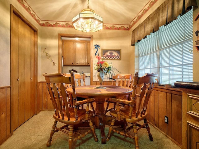 dining area featuring an inviting chandelier, light tile patterned flooring, and wood walls