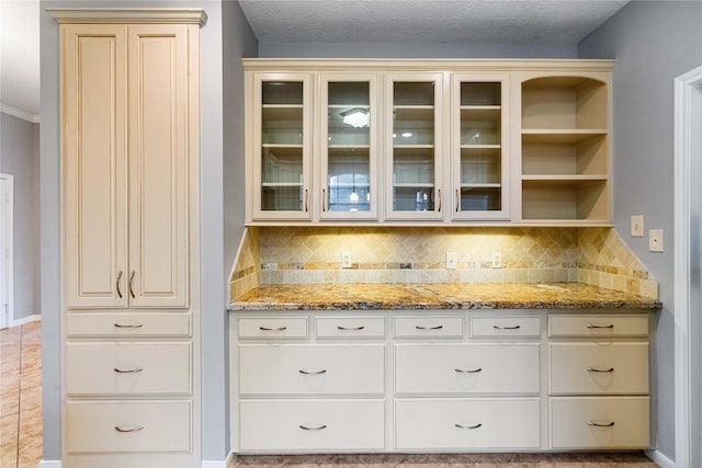 bar with light stone counters, decorative backsplash, and cream cabinetry