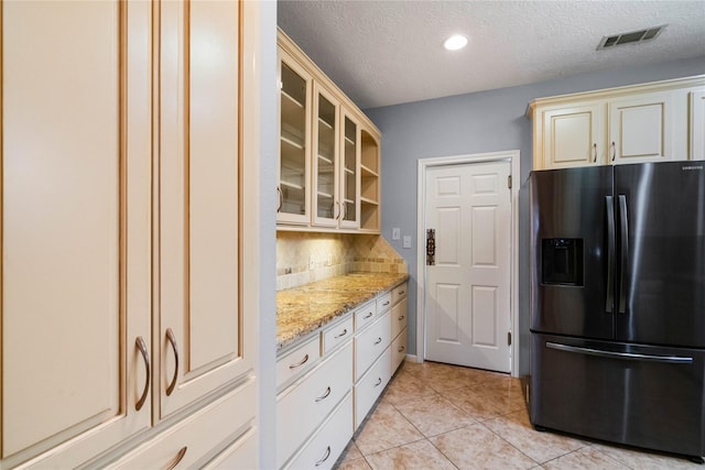 kitchen featuring tasteful backsplash, stainless steel fridge with ice dispenser, light tile patterned floors, light stone countertops, and cream cabinetry