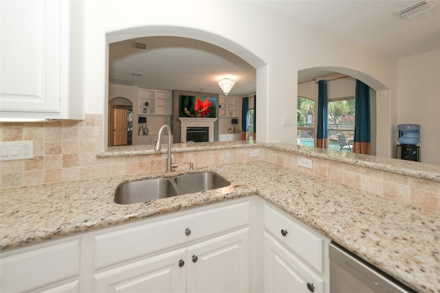 kitchen featuring white cabinetry, sink, stainless steel dishwasher, and light stone countertops