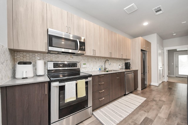 kitchen with sink, stainless steel appliances, decorative backsplash, light wood-type flooring, and light brown cabinets