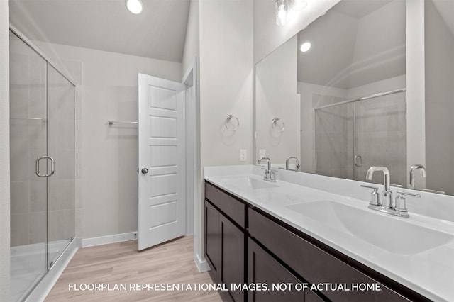 bathroom featuring double vanity, wood finished floors, a sink, and a shower stall