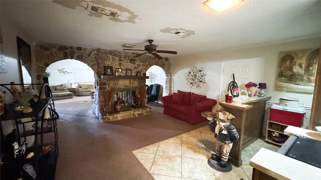 living room featuring ceiling fan, a stone fireplace, light carpet, and a textured ceiling