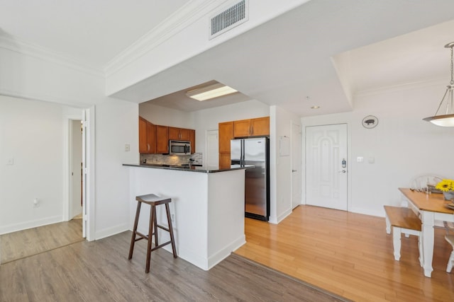 kitchen with crown molding, hanging light fixtures, kitchen peninsula, stainless steel appliances, and light hardwood / wood-style floors