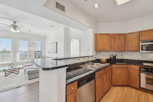 kitchen featuring appliances with stainless steel finishes, tasteful backsplash, sink, light hardwood / wood-style floors, and kitchen peninsula