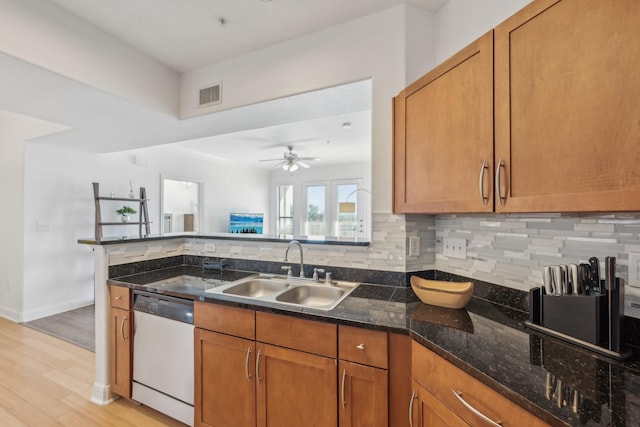 kitchen with sink, tasteful backsplash, light hardwood / wood-style flooring, dark stone countertops, and dishwasher