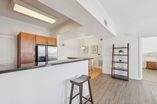 kitchen with a breakfast bar area, crown molding, light hardwood / wood-style flooring, stainless steel fridge, and pendant lighting