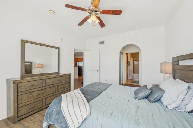 bedroom with crown molding, stainless steel refrigerator, ceiling fan, ensuite bathroom, and light hardwood / wood-style floors