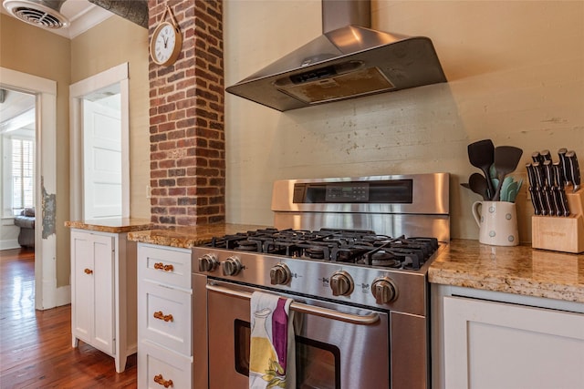 kitchen with light stone counters, white cabinets, stainless steel range with gas stovetop, and wall chimney exhaust hood