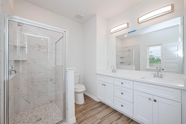 bathroom featuring wood-type flooring, tiled shower, vanity, and toilet