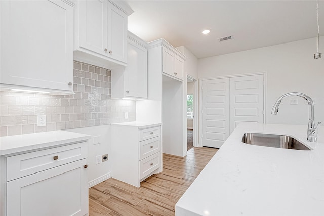 kitchen featuring light wood-type flooring, sink, decorative backsplash, and white cabinets