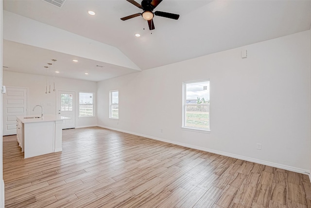 unfurnished living room featuring lofted ceiling, sink, a wealth of natural light, and light hardwood / wood-style flooring