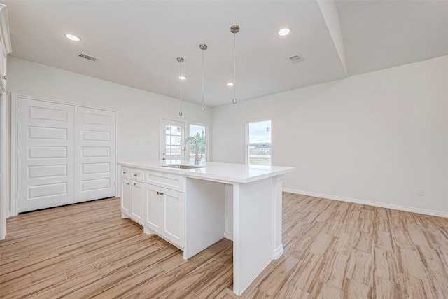 kitchen with decorative light fixtures, white cabinetry, an island with sink, sink, and light wood-type flooring