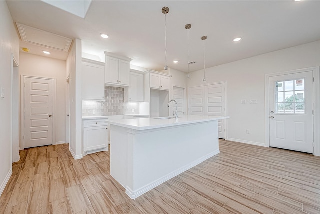 kitchen with decorative backsplash, white cabinets, a center island with sink, decorative light fixtures, and light wood-type flooring