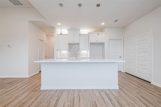 kitchen featuring sink, tasteful backsplash, light wood-type flooring, an island with sink, and white cabinets