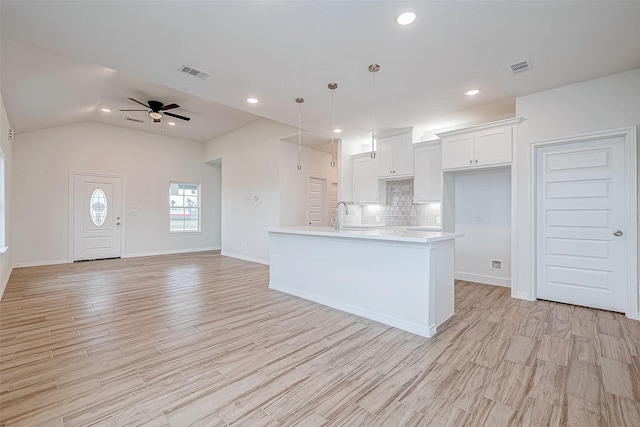 kitchen featuring tasteful backsplash, white cabinets, a center island with sink, decorative light fixtures, and light wood-type flooring