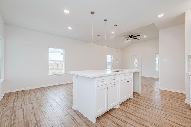 kitchen featuring pendant lighting, sink, white cabinetry, a center island with sink, and light wood-type flooring