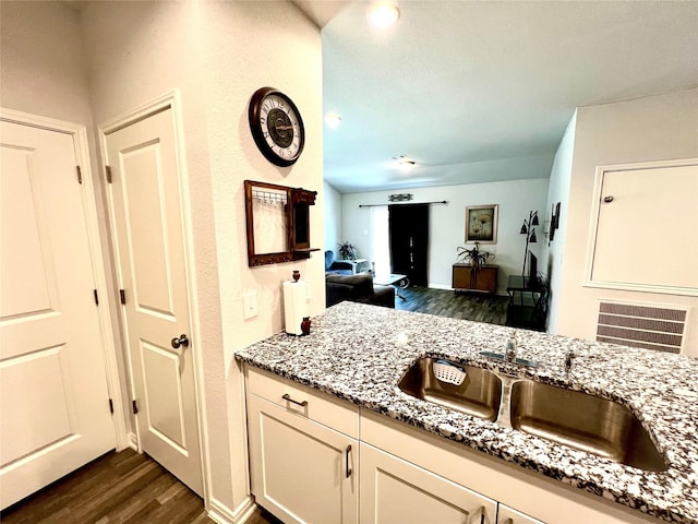 kitchen with light stone counters, sink, white cabinetry, and dark hardwood / wood-style flooring