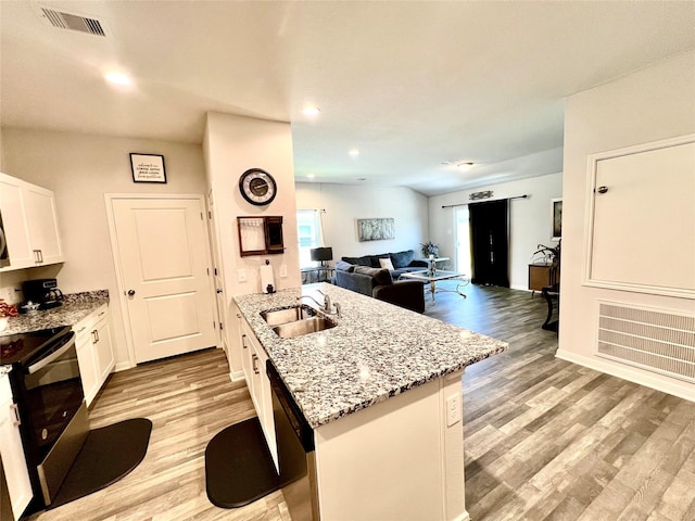 kitchen featuring stainless steel range with electric stovetop, sink, white cabinets, and a center island with sink