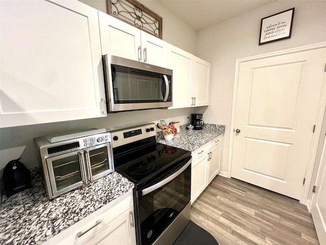 kitchen with light stone counters, light wood-type flooring, white cabinets, and appliances with stainless steel finishes