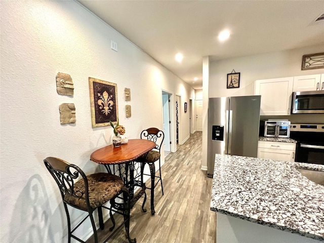 kitchen with sink, stone counters, appliances with stainless steel finishes, white cabinets, and light wood-type flooring