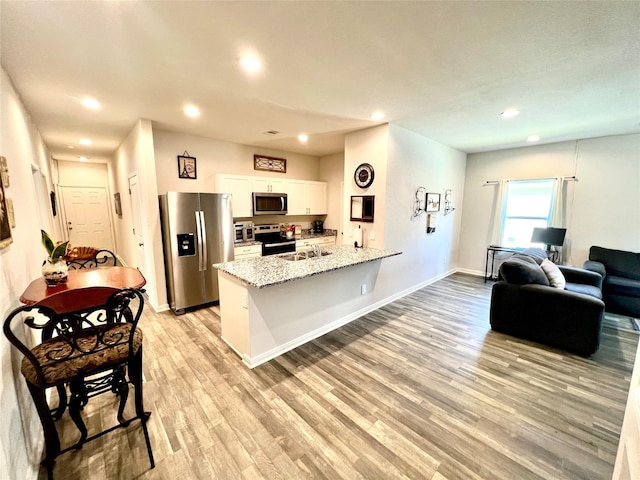 kitchen featuring light stone countertops, white cabinetry, appliances with stainless steel finishes, and light hardwood / wood-style flooring