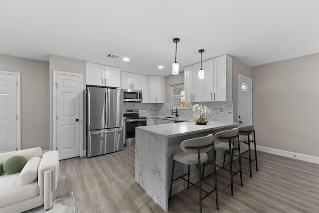 kitchen featuring a breakfast bar area, decorative light fixtures, stainless steel appliances, light stone countertops, and white cabinets