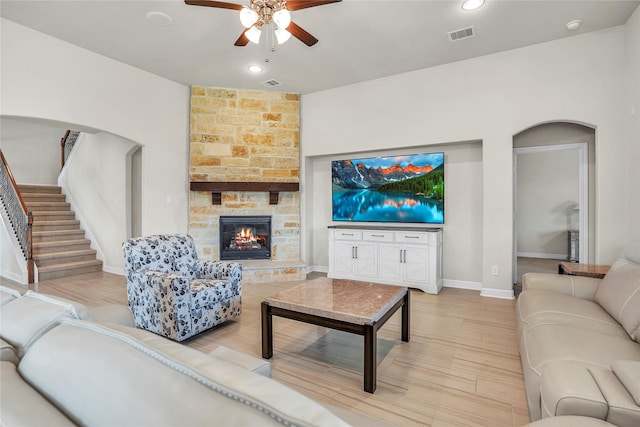 living room featuring a fireplace, ceiling fan, and light wood-type flooring