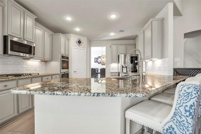 kitchen with gray cabinets, appliances with stainless steel finishes, stone countertops, and kitchen peninsula