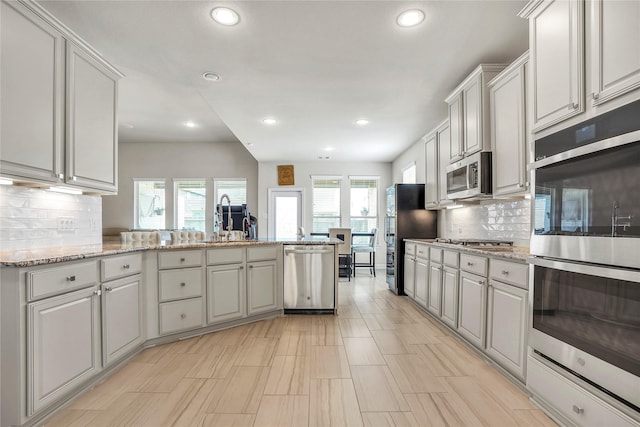 kitchen featuring light stone counters, stainless steel appliances, sink, and a wealth of natural light