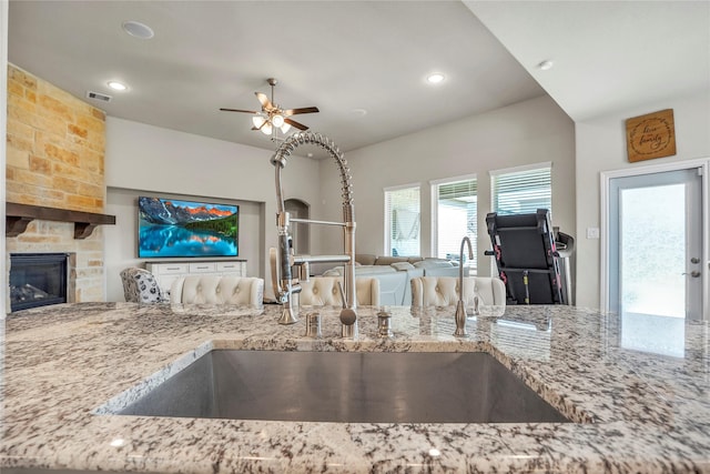 kitchen featuring light stone counters, sink, a fireplace, and ceiling fan