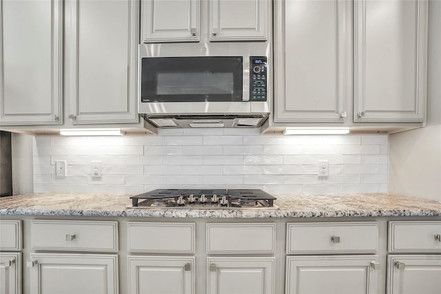 kitchen with white cabinetry, stainless steel appliances, light stone countertops, and backsplash