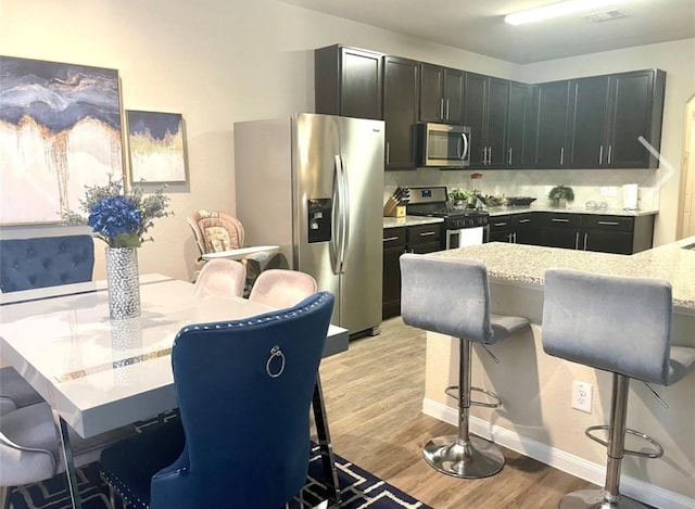 kitchen featuring a breakfast bar, stainless steel appliances, light hardwood / wood-style floors, light stone countertops, and decorative backsplash