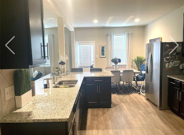 kitchen featuring sink, kitchen peninsula, stainless steel refrigerator with ice dispenser, light stone countertops, and light wood-type flooring