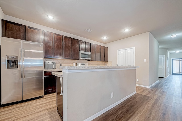 kitchen featuring appliances with stainless steel finishes, decorative backsplash, a center island, dark brown cabinets, and light hardwood / wood-style flooring