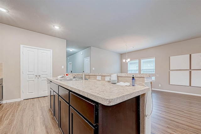 kitchen featuring decorative light fixtures, sink, a kitchen island with sink, light hardwood / wood-style floors, and dark brown cabinetry