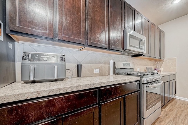 kitchen featuring dark brown cabinetry, backsplash, light wood-type flooring, and appliances with stainless steel finishes