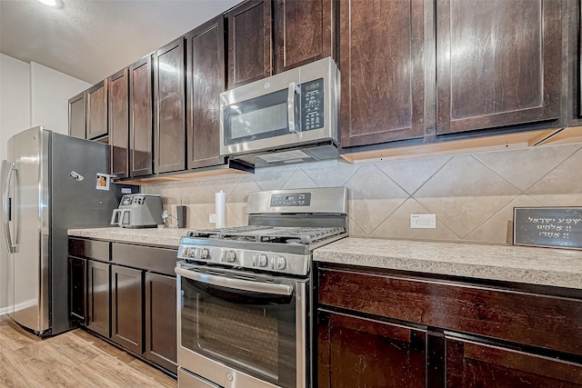 kitchen with appliances with stainless steel finishes, dark brown cabinets, backsplash, and light wood-type flooring