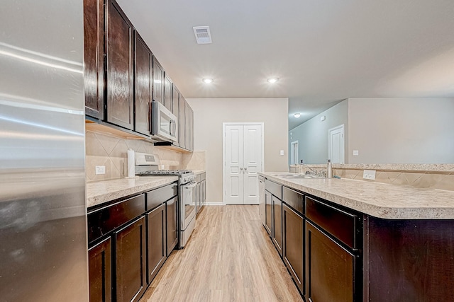 kitchen featuring appliances with stainless steel finishes, a kitchen island with sink, sink, and dark brown cabinets