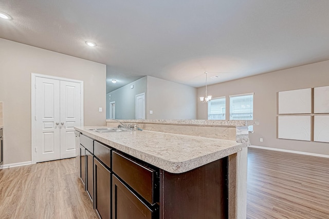 kitchen featuring decorative light fixtures, sink, a kitchen island with sink, light hardwood / wood-style floors, and dark brown cabinetry