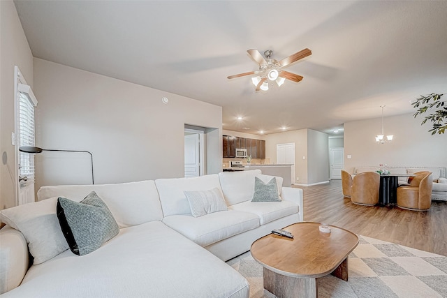 living room with ceiling fan with notable chandelier and light wood-type flooring