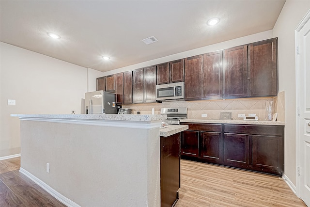 kitchen featuring dark brown cabinetry, tasteful backsplash, light hardwood / wood-style flooring, an island with sink, and stainless steel appliances