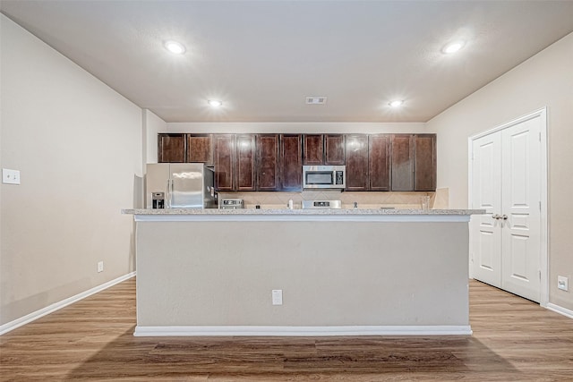 kitchen with dark brown cabinetry, stainless steel appliances, light hardwood / wood-style floors, and a center island with sink