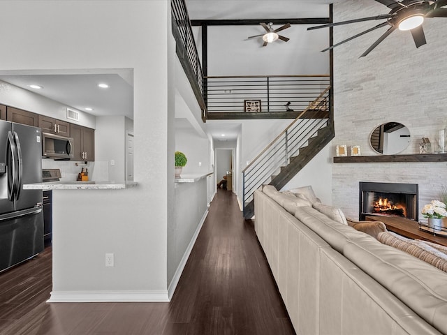 living room featuring a high ceiling, ceiling fan, a stone fireplace, and dark hardwood / wood-style flooring