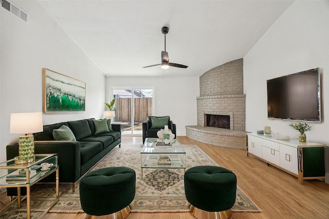 living room featuring vaulted ceiling, ceiling fan, a fireplace, and light hardwood / wood-style floors