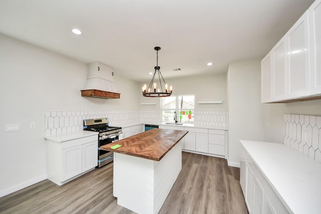 kitchen featuring butcher block countertops, white cabinets, hanging light fixtures, a center island, and stainless steel gas range oven