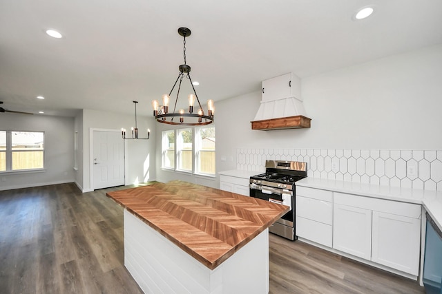 kitchen featuring dark hardwood / wood-style floors, pendant lighting, stainless steel gas stove, white cabinetry, and backsplash