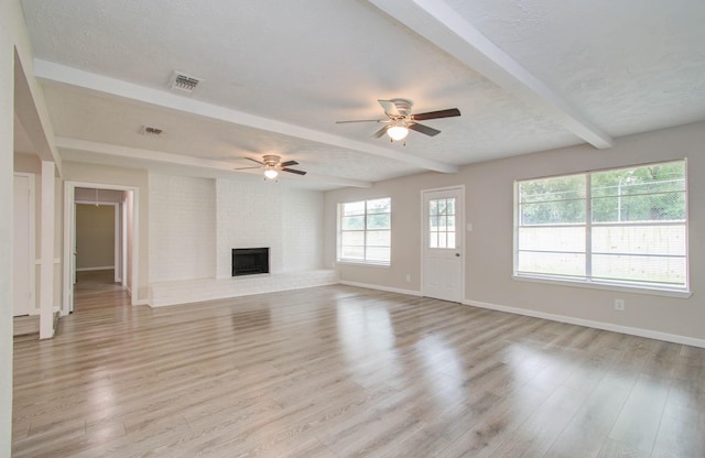 unfurnished living room featuring light hardwood / wood-style flooring, ceiling fan, a textured ceiling, a brick fireplace, and beamed ceiling