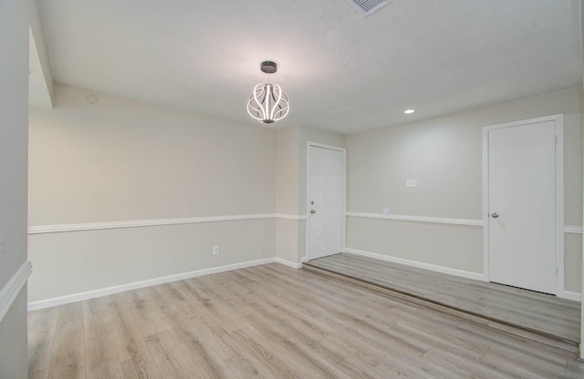 unfurnished room featuring a notable chandelier and light wood-type flooring