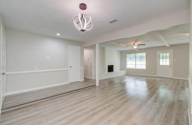 unfurnished living room with a brick fireplace, light hardwood / wood-style flooring, a textured ceiling, beamed ceiling, and ceiling fan